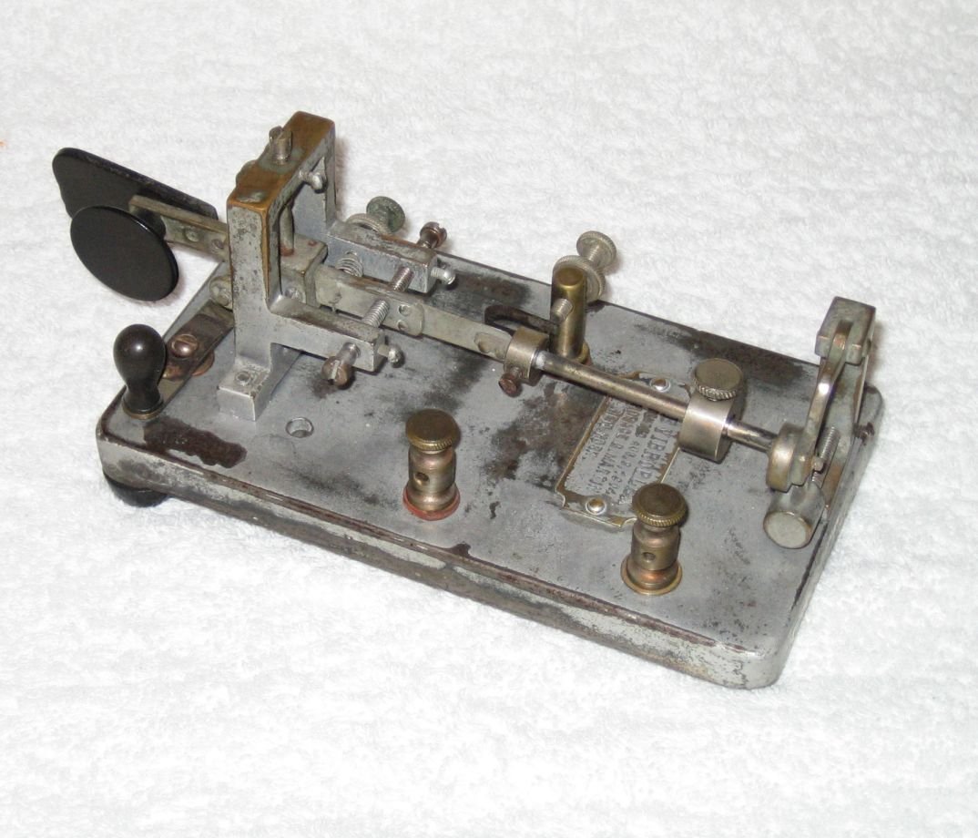 Figure 3 — The same mechanism in the metal — a real Vibroplex, top-down: the pendulum and its cylindrical weight, the contacts, the pivot, and the paddle. Compare it to the schematic above. (Wikimedia Commons…