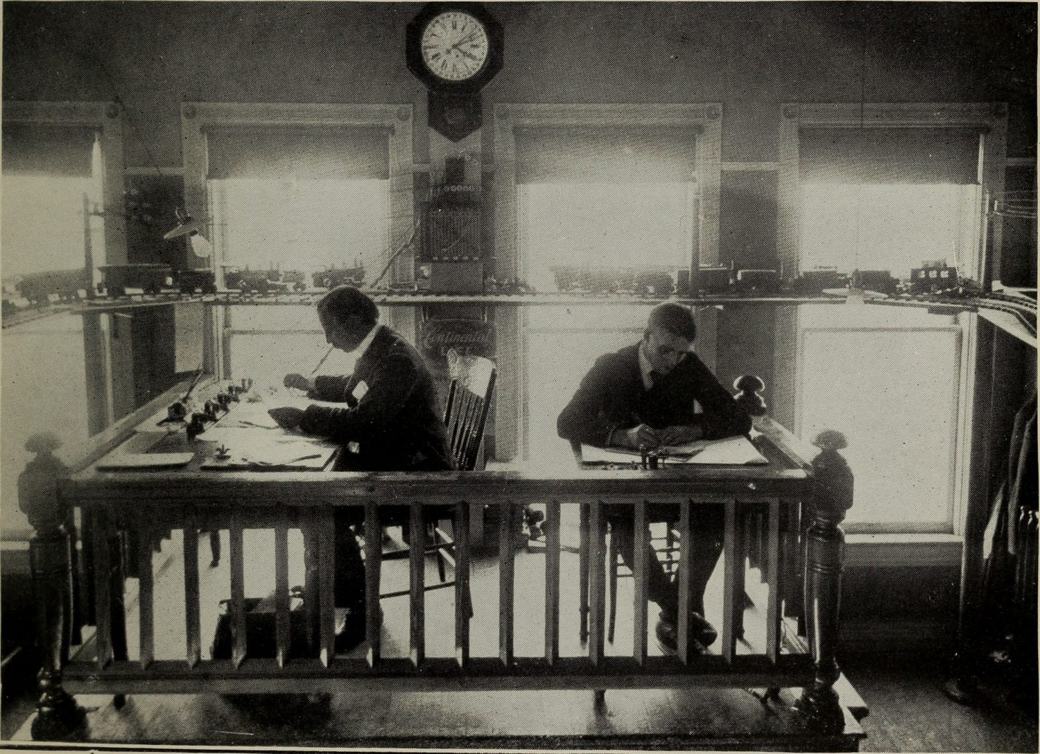 Figure 4 — Operators receiving by ear at a railroad telegraph desk — the human reality behind all the brass. No reading of tape: just a hand ready to write and an ear trained on the sounder's clicks (a resona…