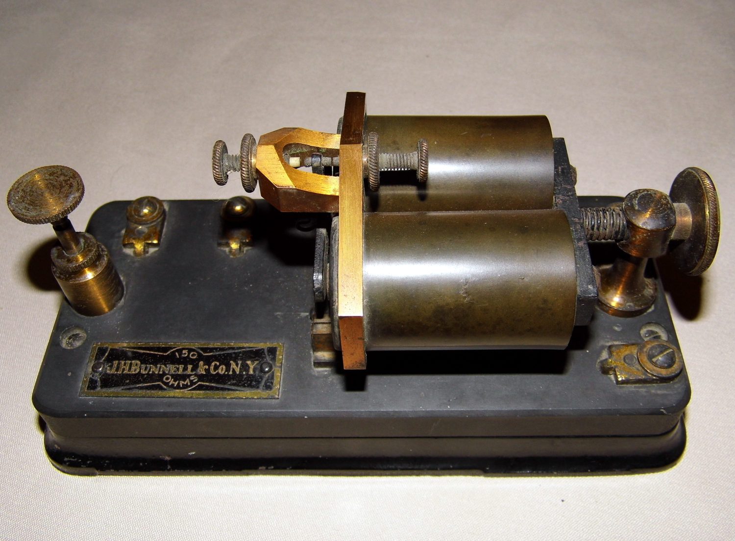 Figure 1 — A J. H. Bunnell & Co. of New York telegraph sounder — the classic receiving instrument of the American landline era, with the maker's nameplate on the base. The twin electromagnet coils sit on the …