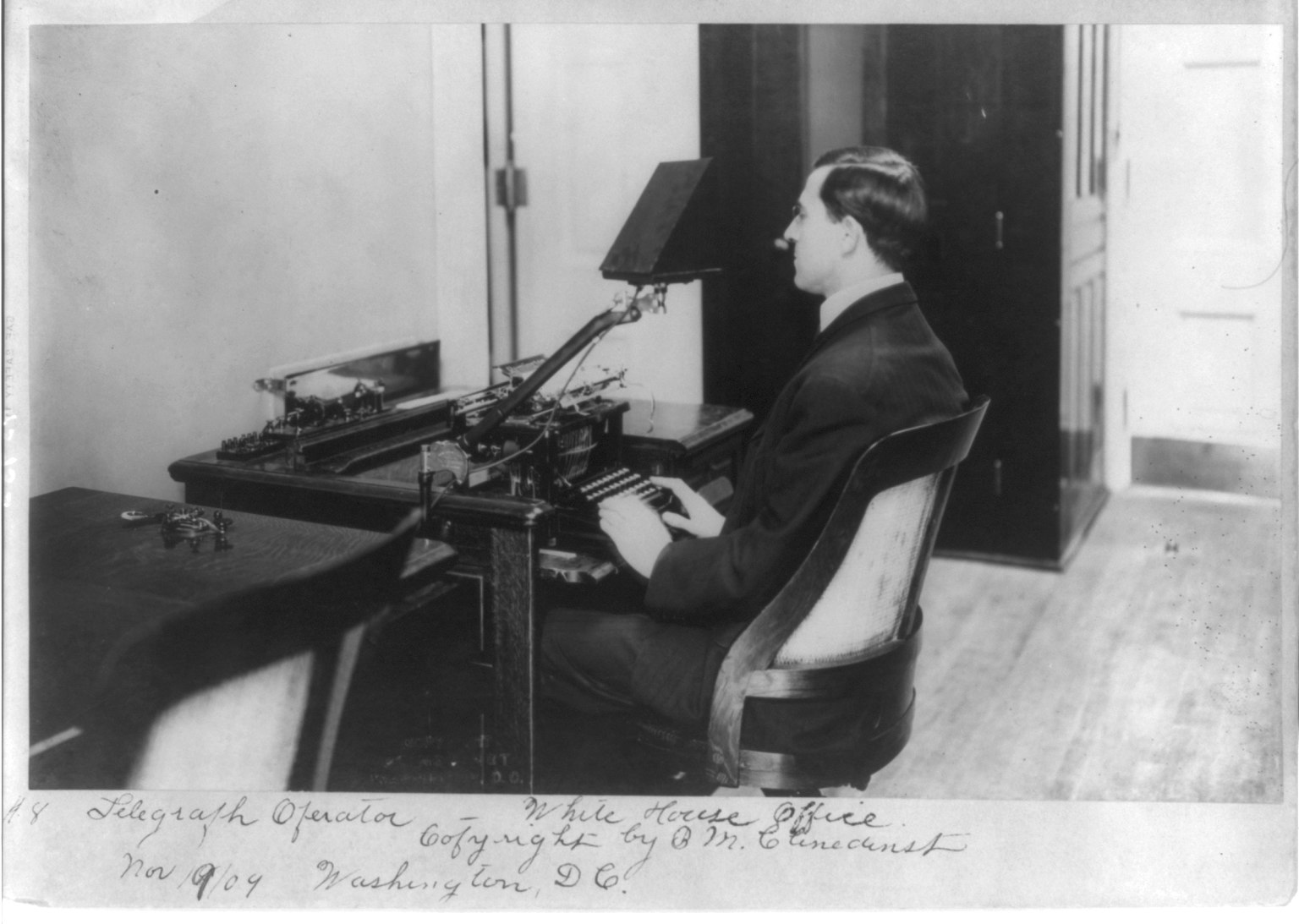 Figure 5 — A telegraph operator at his position — the everyday reality behind the grand history. A desk of keys, sounders, and relays, a message blank, and a trained hand and ear. Multiply this by tens of tho…