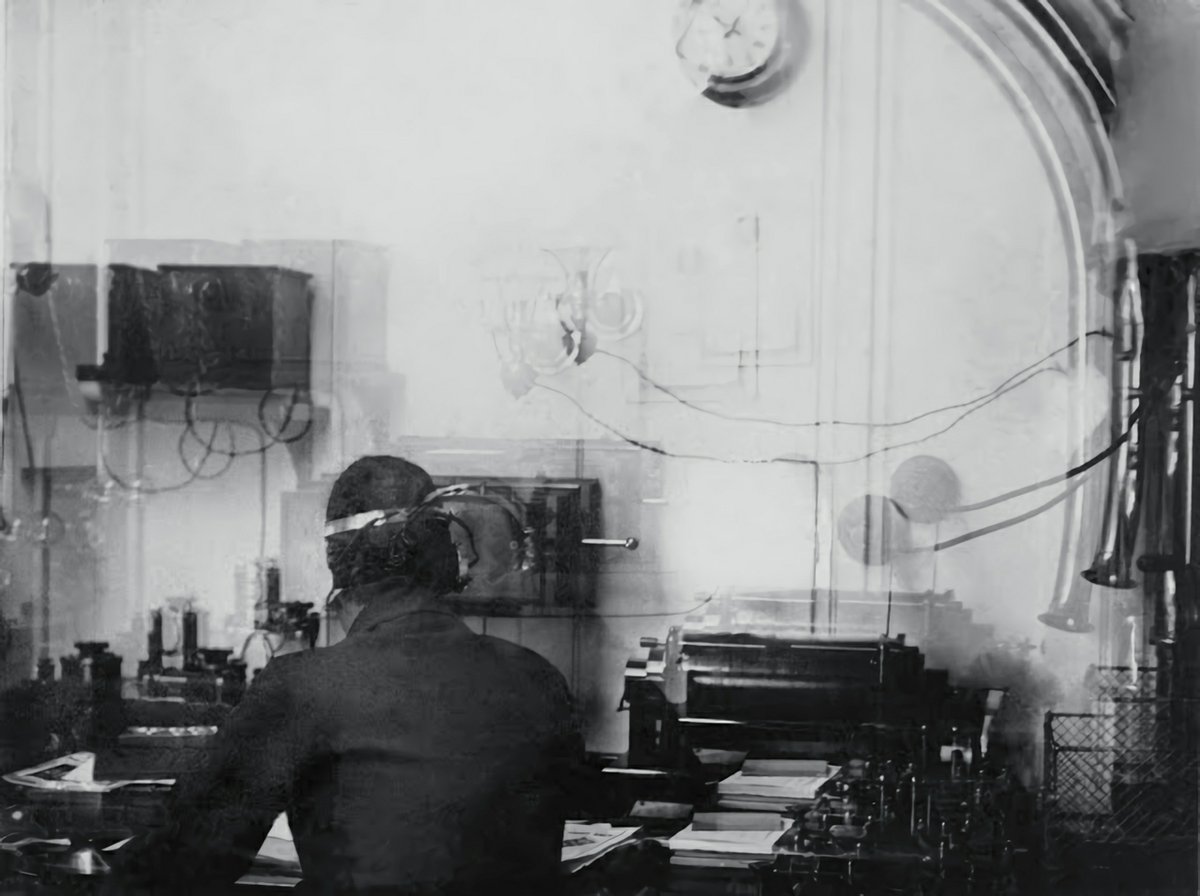 Figure 2 — The Marconi wireless room aboard the Titanic, operator Harold Bride at the desk — the only known photograph of the room from which Phillips and Bride sent CQD and then SOS into the North Atlantic n…